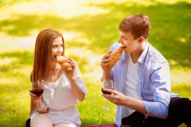 Sevecen genç bir çift kruvasan yiyor ve parkta piknik yaparken şarap içiyor.