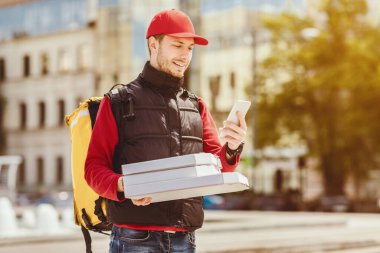 Kurye telefon kullanıyor pizza dağıtıyor ve şehirde açık havada restoranda yemek ısmarlıyor. Yemek teslimatı konsepti. Boşluğu Kopyala