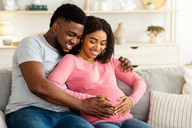 Güzel bir gülümseme, Afrikalı ailelerin evdeki koltukta oturup hamile bir kadının karnına dokunmasını bekliyor.