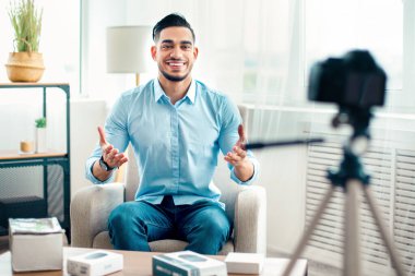 Genç bir Arap girişimci, teknoloji ürünleri ve rahat bir atmosferle çevriliyken kamerayı kendine güvenle kendine bağlar. Profesyonellik ve coşku yayıyor..