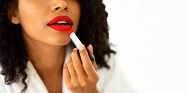 Günlük makyaj. Bornozlu tanınmayan siyahi kadın pembe ruj sürüyor, evde dudaklarıyla ilgileniyor, kesilmiş görüntü, yakın plan.