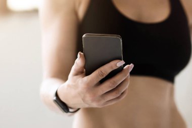 Zayıf vücut, formda model, orta yaşlı antrenör ve modern teknoloji. Spor giyim sektöründe kaslı olgun bir kadın akıllı telefona bakıyor ve mesaj veya spor blogu okuyor, kırpılmış, boş alan