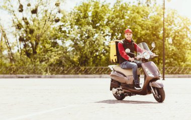 Kurye, kutuda yiyecek getiriyor motosikletle dışarı çıkıyor, kameraya gülümsüyor. Boş Alan