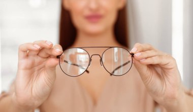Bir kadın gözlüklerine odaklanır ve onları gözünün önünde tutar. İyi aydınlatılmış bir odada beliriyor. Rahatlamış bir atmosfer ve gündüz aktivitesi olduğunu gösteriyor..