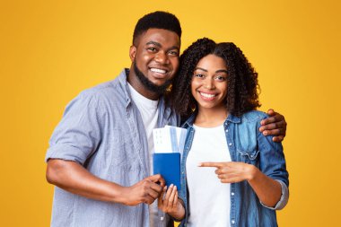 Neşeli bir çift birlikte poz veriyor, pasaportlarını gösteriyorlar, yaklaşan seyahatleri için heyecanlılar. Parlak sarı bir arka planla gelişigüzel giyinmişler. Mutluluklarını arttırıyorlar..