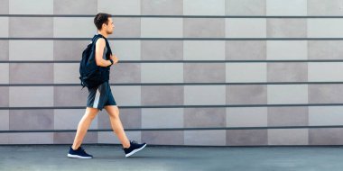 Sabah antrenmanına git. Spor giyimli, spor ayakkabılı, sırt çantalı, gri duvarlı arka plan, yan manzara, boş alan.