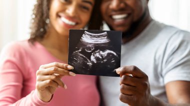 Mutlu bir siyahi çift, bebeklerinin ultrason görüntülerini yakından gösteriyor.