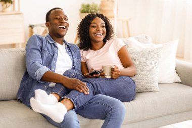 Neşeli Afrikalı erkek ve kadın çay içip evde film izliyorlar, birlikte eğleniyorlar, mekanı kopyalıyorlar.