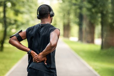 Spor giyimli siyah bir adamın park yerinde dikilip yaralı sırtına dokunuşunun arkası.