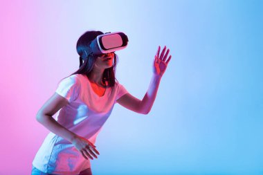 Bir kadın sanal gerçeklikle ilgilenir, kulaklık takar ve dijital bir çevreyi keşfeder. Parlak pembe ve mavi ışıklar teknolojik etkinliğin büyüleyici atmosferini arttırır..