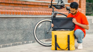 Siparişi termal çantaya koyuyorum. Bisikletli sakallı kurye, sokaktaki büyük sarı çantaya bakar.