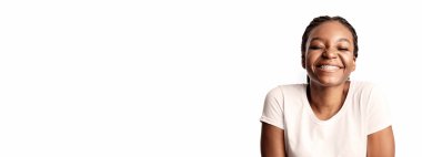 Beyaz tişört giyen neşeli genç bir kadın gülümseyerek mutluluğunu sergiliyor. Düz arkaplan onun parlak ifadesini ve pozitif enerjisini vurguluyor..