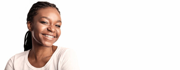 A young woman with braided hair smiles brightly, showcasing her braces. She exudes confidence and joy, set against a clean white background that emphasizes her expression.