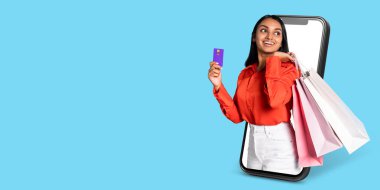 Alıcı, akıllı telefon ekranı ile iletişim kurarken elinde bir ödeme kartı ve alışveriş torbası tutmaktan mutluluk duyar. Arkaplan açık mavi, çevrimiçi perakende faaliyetlerini vurguluyor.