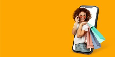 Mutlu bir müşteri internet üzerinden alışveriş yapmak için akıllı telefon kullanıyor, bir elinde alışveriş torbaları, canlı bir ortamda dijital ticaretin kolaylığını gösteriyor..