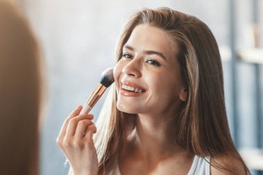 Güzellik ve makyaj konsepti. Evdeki aynanın yanında yüzü kızaran güzel bir kadın.