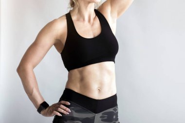 Egzersiz yaptıktan sonra rahatla, nefeslen, evde ya da kendi kendini izole ederken spor salonuna ara ver. Spor giyimli, kaslı, orta yaşlı kadın spor kıyafetleri içinde spor takip cihazı ile alnındaki teri siliyor.