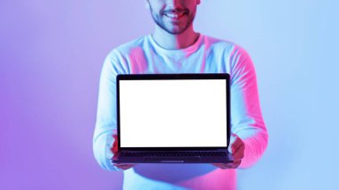 Genç bir adam önünde boş bir laptop tutuyor, parlak bir şekilde gülümsüyor. Arka planda canlı mavi ve mor ışıklar var, modern ve enerjik bir atmosfer yaratıyor..