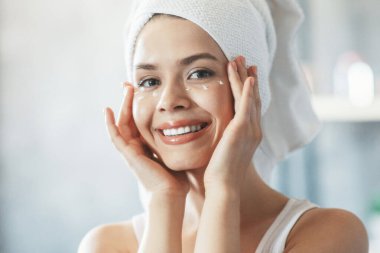 Güzel bir kız mükemmel cildine göz kremi sürerek banyo yaptıktan sonra içeride aynanın yanında.