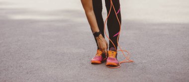 Kardiyo eğitimi ve atletizm. Spor kıyafetli Afro-Amerikan kadın spor ayakkabıları spor salonunda spor yaparken spor ayakkabılarını düzeltiyor. Açık havada ip atlama, kırpma, panorama...