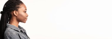 Genç bir kadın, kot ceket giyerken örgülü saç stilini gösteriyor. Tarafsız arkaplan yansıtıcı bir anda onun özelliklerini ve ifadesini vurgular..