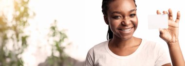 Neşeli bir kadın aydınlık bir odada elinde kocaman bir gülümsemeyle boş bir kart tutuyor. Arka plandaki yeşillik davetkar atmosfere taze bir dokunuş katıyor..