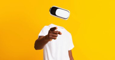 Bir kullanıcı sanal gerçekliğe dalıp, kulaklık takarken tek eliyle işaret eder. Canlı sarı arka plan gelişmiş gerçeklik keşiflerinde kullanılan modern teknolojiyi vurguluyor..