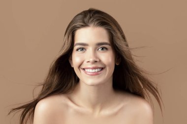 İpeksi uzun saçlı, temiz tenli, kameraya bakan ve kahverengi arka planda gülümseyen güzel bir kadın model. Vücuduyla ilgilenen havluyla seksi bir kadın. Güzellik ve refah kavramı