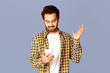 Heyecanlı Hintli adam elinde menekşe arkaplan ve panorama ile akıllı telefona bakıyor.