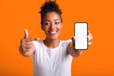 Seç bunu. Siyah kadın cep telefonuyla beyaz beyaz ekran, turuncu duvar ve boş alan sunuyor.