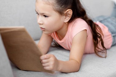 Evdeki koltukta kitap okuyan küçük Asyalı kız. Çocuk Haftasonu Tatili. Seçici Odaklanma