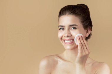 Kusursuz cildi olan güzel bir genç kız. Yüzünü tonik ya da bej arka planda mikiler suyuyla temizliyor.