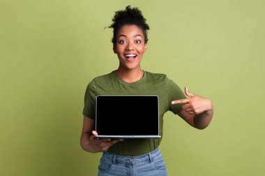 Heyecanlı Afrikalı kız laptopunu siyah boş ekranla sunuyor. Model için. Yeşil stüdyo duvarında izole edilmiş.
