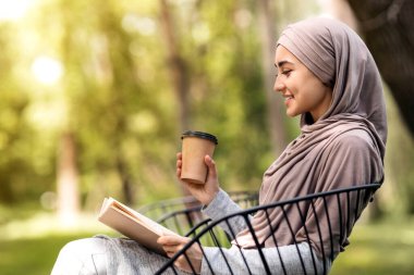 Arap kızın kitap okuduğu ve şehir parkında kahve içtiği profil fotoğrafı.