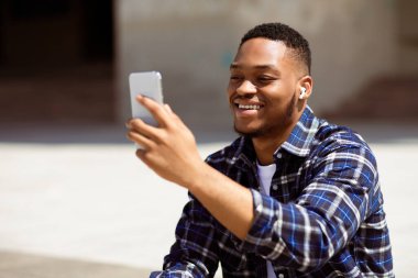 Yakışıklı siyahi adamın cep telefonuyla video görüşmesi yaparken, bir şey izlerken ya da parkta selfie çekerken portresi.
