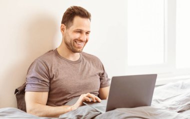Evden Çalışmak. Neşeli Adam Laptop kullanıyor Uzaktan kumandalı çalışıyor Yatakta Kapalı Oturuyor. Serbest Çalışan Adam Yatak Odası 'nda İnternet' e göz atıyor. Mesafe Görevi, Serbest Yaşam Tarzı.