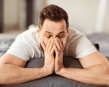 Uykusuzluk Konsepti. Uykucu adam gözlerini ovuşturuyor, uyanıyor. Evde yatakta karnı üzerinde yatıyor..