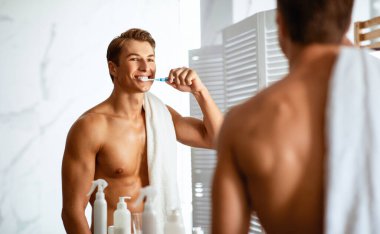 Ağız temizliği ve diş bakımı konsepti. Diş fırçasıyla dişlerini fırçalayan adam aynaya bakıyor.