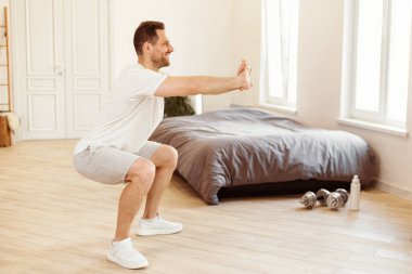 Evde iki bacaklı çömelme egzersizi yapan bir adam. Sportif Yaşam Tarzı, Erkek Sporu Rutin Konsepti. Sabahları yatak odasında egzersiz yapan adam. Metin için Boşluk