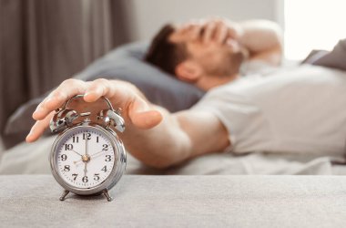 Kötü Uyku. Uykucu adam alarmlı saati kapatıyor. Evde, yatakta uyanıyor. Sığ Derinlik, Seçici Odaklanma