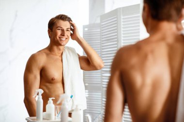 Sabah rutini. Yakışıklı genç adam elleriyle saçlarına dokunuyor ve aynanın karşısında dikilirken gülümsüyor.