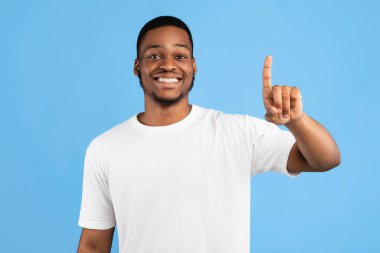 İlk olarak. Siyah adam bir numarayı gösteriyor. Mavi arka planda kameraya gülümsüyor. Stüdyo Çekimi