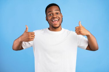 Siyahi Milenyum Adamı, stüdyoda mavi arka planda kameraya gülümseyen iki eliyle baş parmağını kaldırıyor.