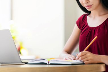 Asyalı güzel kız kafeteryada dizüstü bilgisayarla ders çalışıyor ve notlar alıyor.