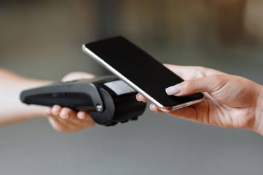 NFC Teknoloji. Tanımlanamayan bir kadın, banka terminalindeki elektronik okuyucuya akıllı telefonuyla ulaşılamayan bir ödeme yapıyor.