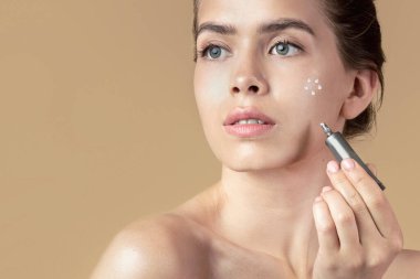 Mükemmel cilt kremi sürmüş seksi genç bir kadın ya da bej arka planda kozmetik fosforlu kalem.