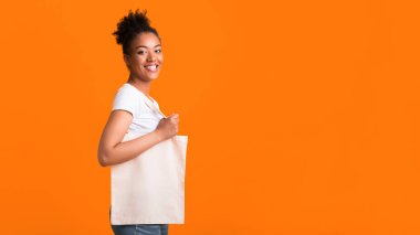 Plastik Kirliliği Durdur. Sarı stüdyo duvarında boş beyaz eko çanta tutan yarı dönüşmüş siyah bir kız. Metin için boş alan