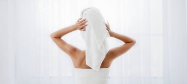 Pencerenin yanında duran, sabah duşundan sonra saçını kurutan kadının arka görüntüsü.