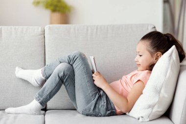 Evdeki koltukta uzanan telefonu kullanan kız. Mobil Oyun ve Çocuklar İçin Aletler Kavramı