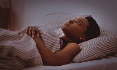 Uykusuzluk, uyku sorunları, sağlık hizmetleri ve yatak uykusu. Depresyondaki genç Afrikalı Amerikalı kadın battaniyeyle yatağa uzanmış, gözleri açık, karanlık yatak odasının içinde, kopya alanı, profil, panorama